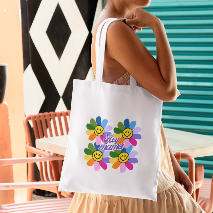 Woman holding a white canvas totebag with hobi vibrant coloured flower design inspired by the work of Takashi Murakami.