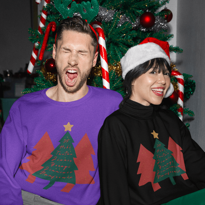 Two people wearing ARMY Holiday Tree BTS Christmas sweaters in front of a decorated Christmas tree, showing festive holiday spirit.