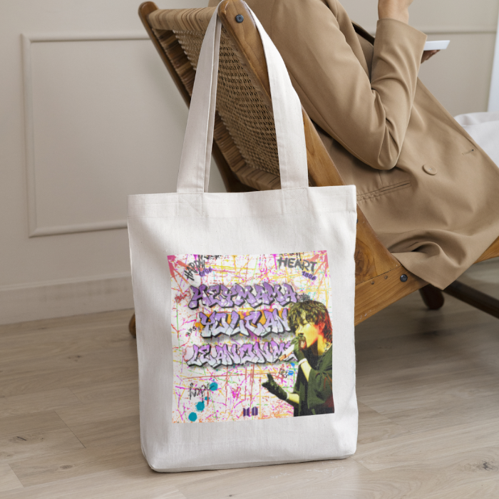 Woman sitting on a chair with beige canvas totebag with J-hope world image and grafitti text Hey mama