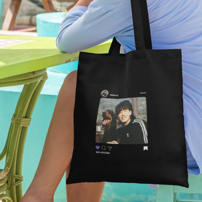 Woman sitting on chair with black canvas totebag BAM JK design instagram