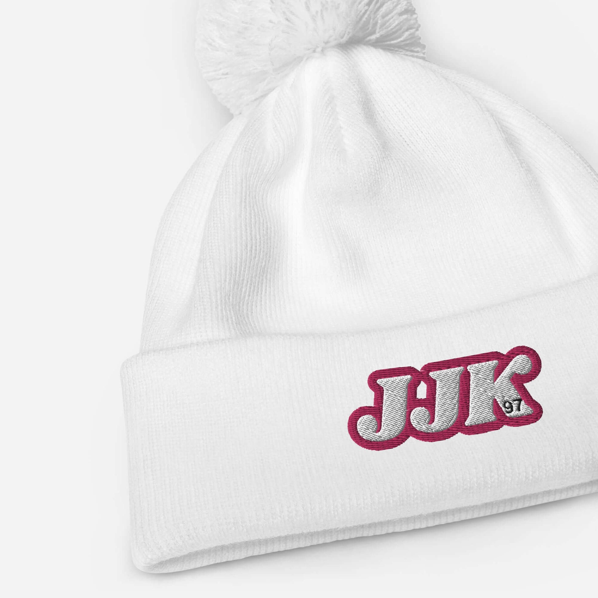 White pom pom beanie with "JJK" embroidery, inspired by Jung Kook. Soft-touch acrylic for warm winter adventures.